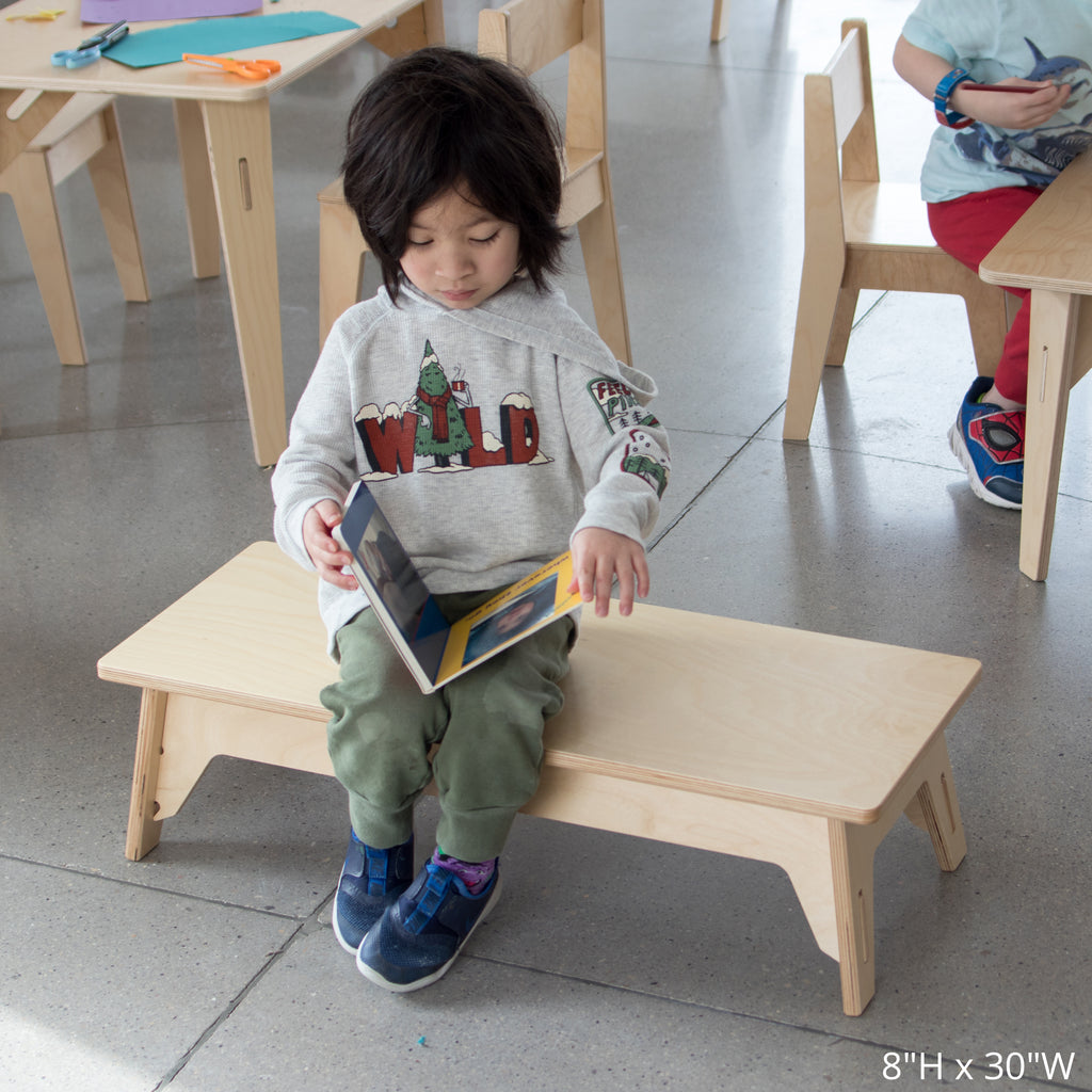 Child reads a book on a 8in high, 30in wide school bench
