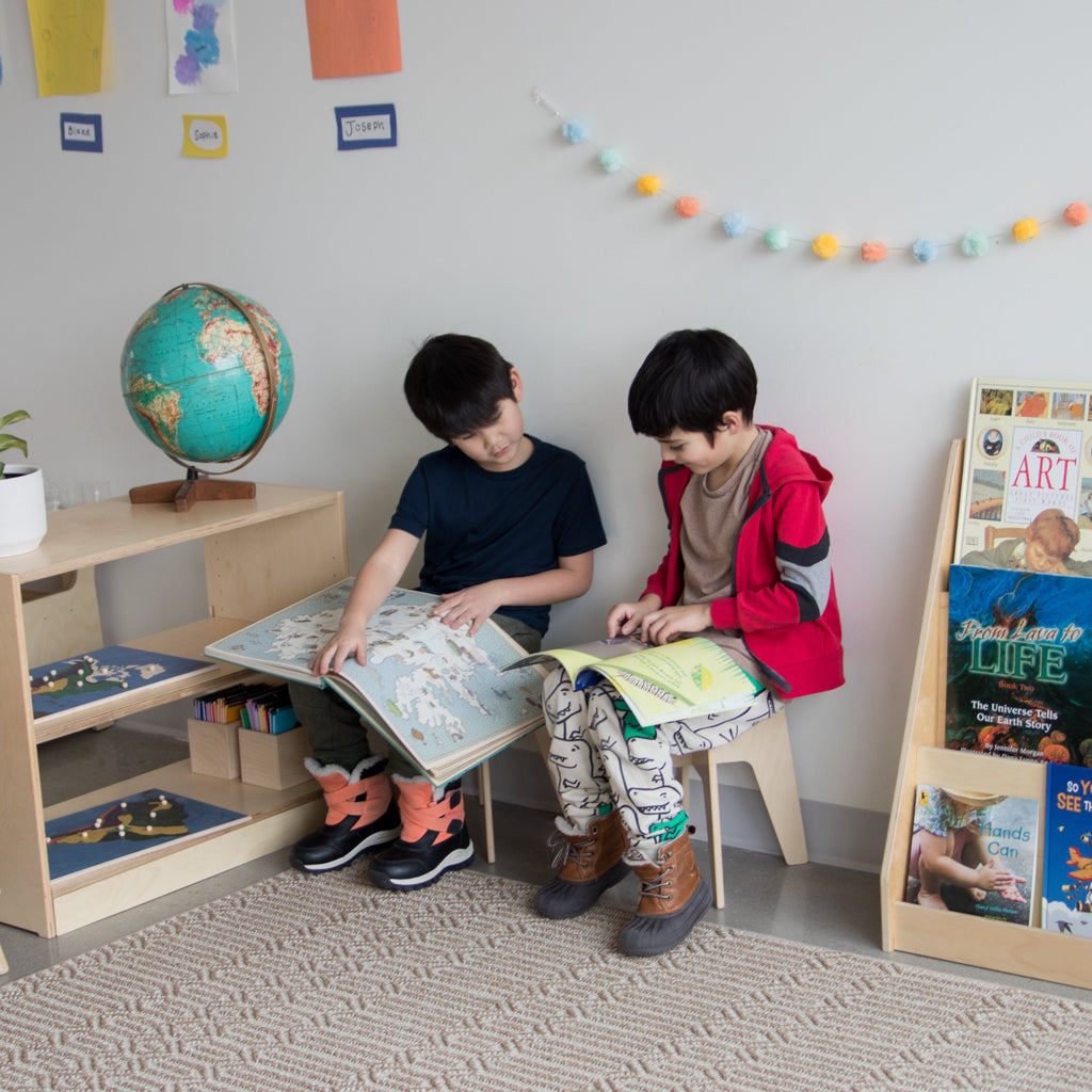 Two young children sit on School Kids Stools and read books in a Montessori environment. 