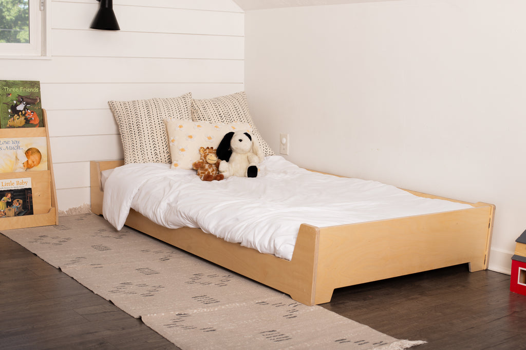 Birch Montessori Floor Bed with stuffed animals and a bookshelf beside it