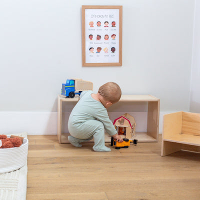 Baby playing with toys in a room with wooden furniture and a framed poster on the wall.