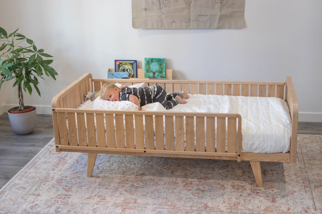 A boy lays on a toddler floor bed with rails including two headboards, one full side and a 3/4 side