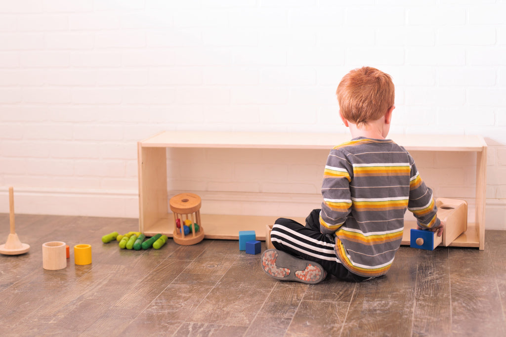 A little boy plays with wooden toys in front of a long infant shelf