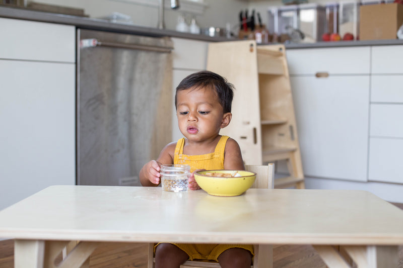 A child sitting at a Wooden Weaning Table