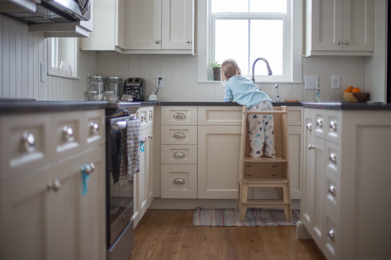 Child standing in a tower at a kitchen counter