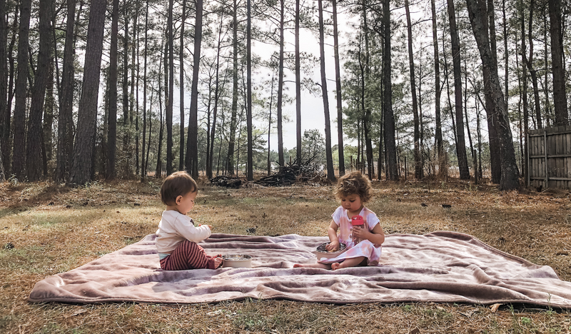 Two children on a blanket in front of trees