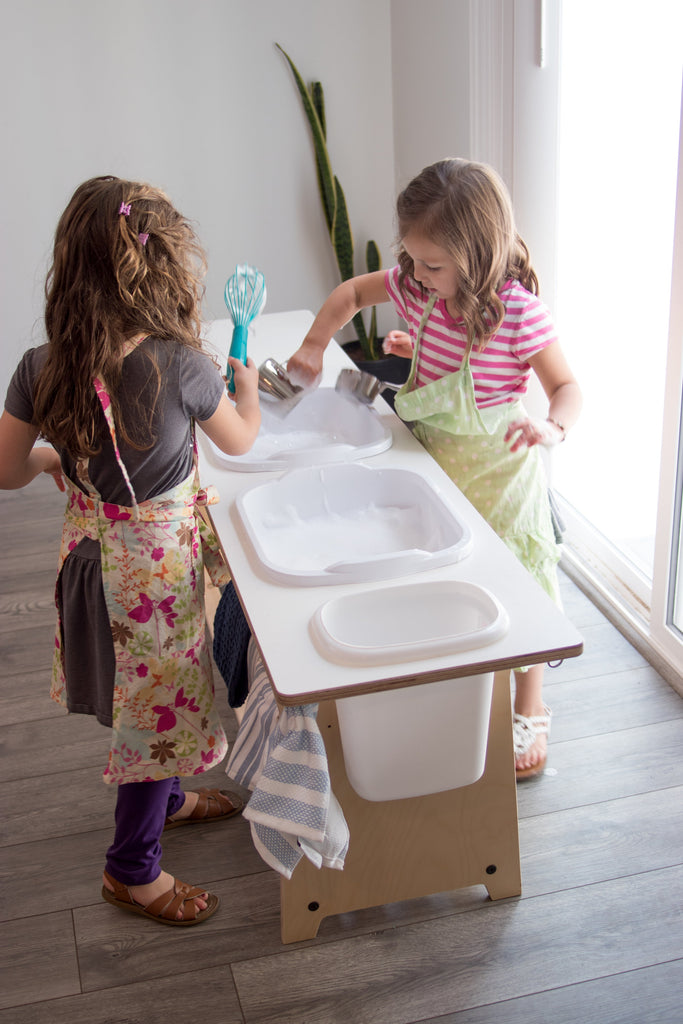 three girls of different ages using a washing station with kitchen tools