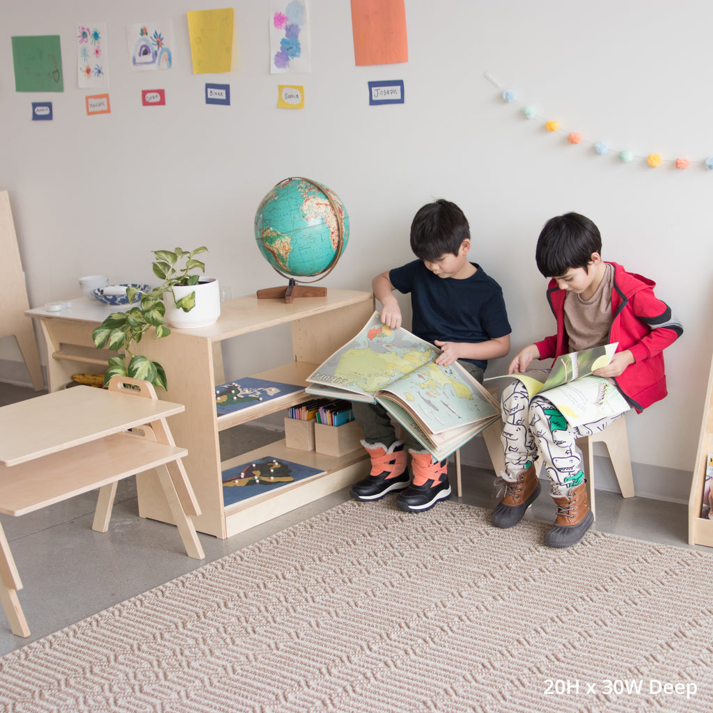 Two children reading books next to a school montessori open back shelf