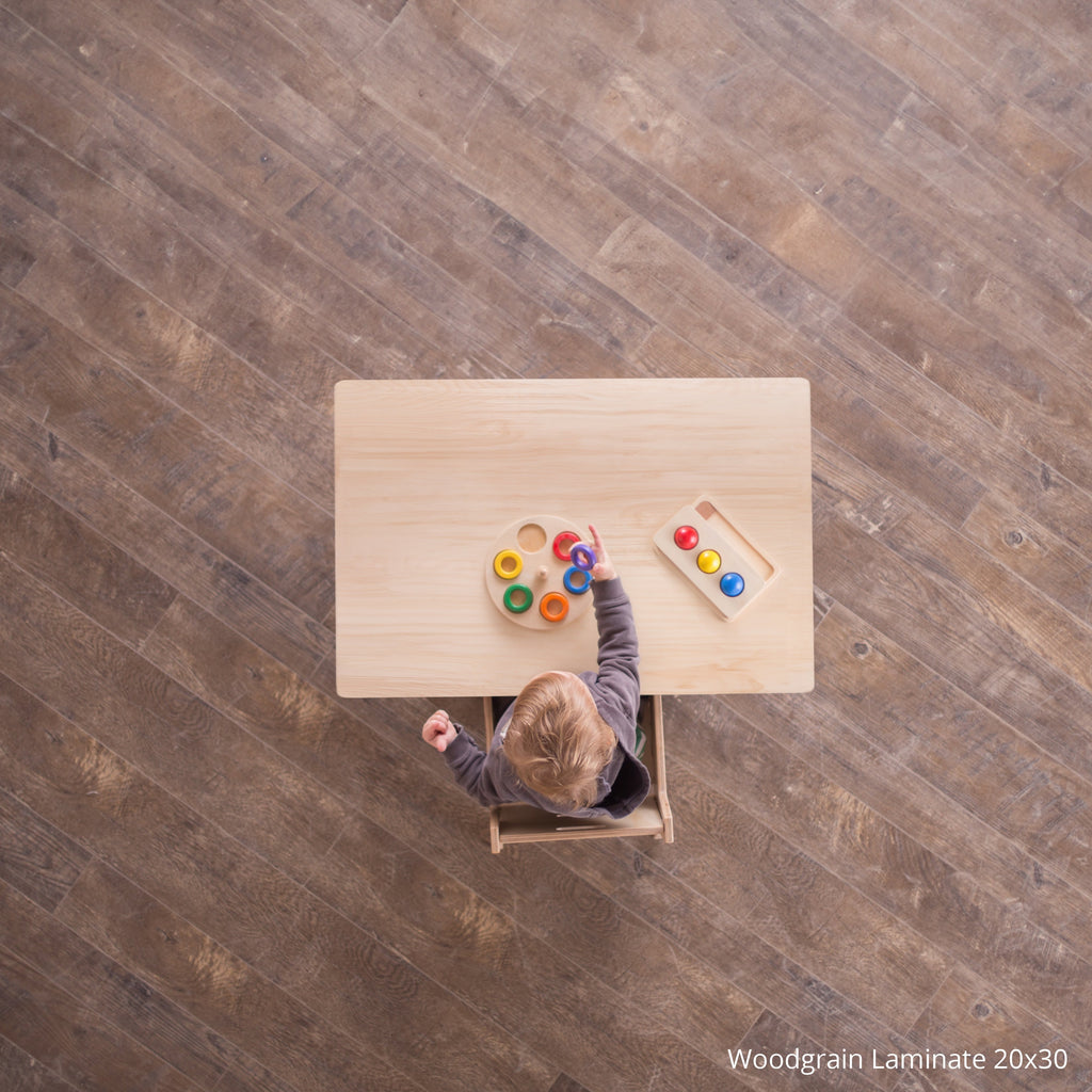 Child playing with colorful toys at a wooden table on a wood-paneled floor.