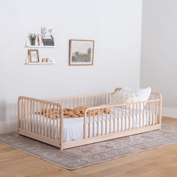 Montessori floor bed with rails with white bedding in a room with a rug and wall decorations.