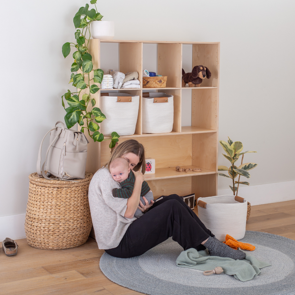 A mother and baby in a cozy nursery setup featuring a Montessori toy shelf with infant essentials. 