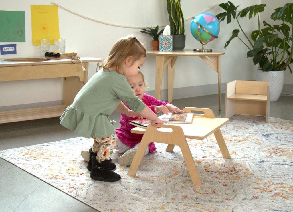 Two toddlers reading books on a Chowki floor table in a Montessori learning environment.