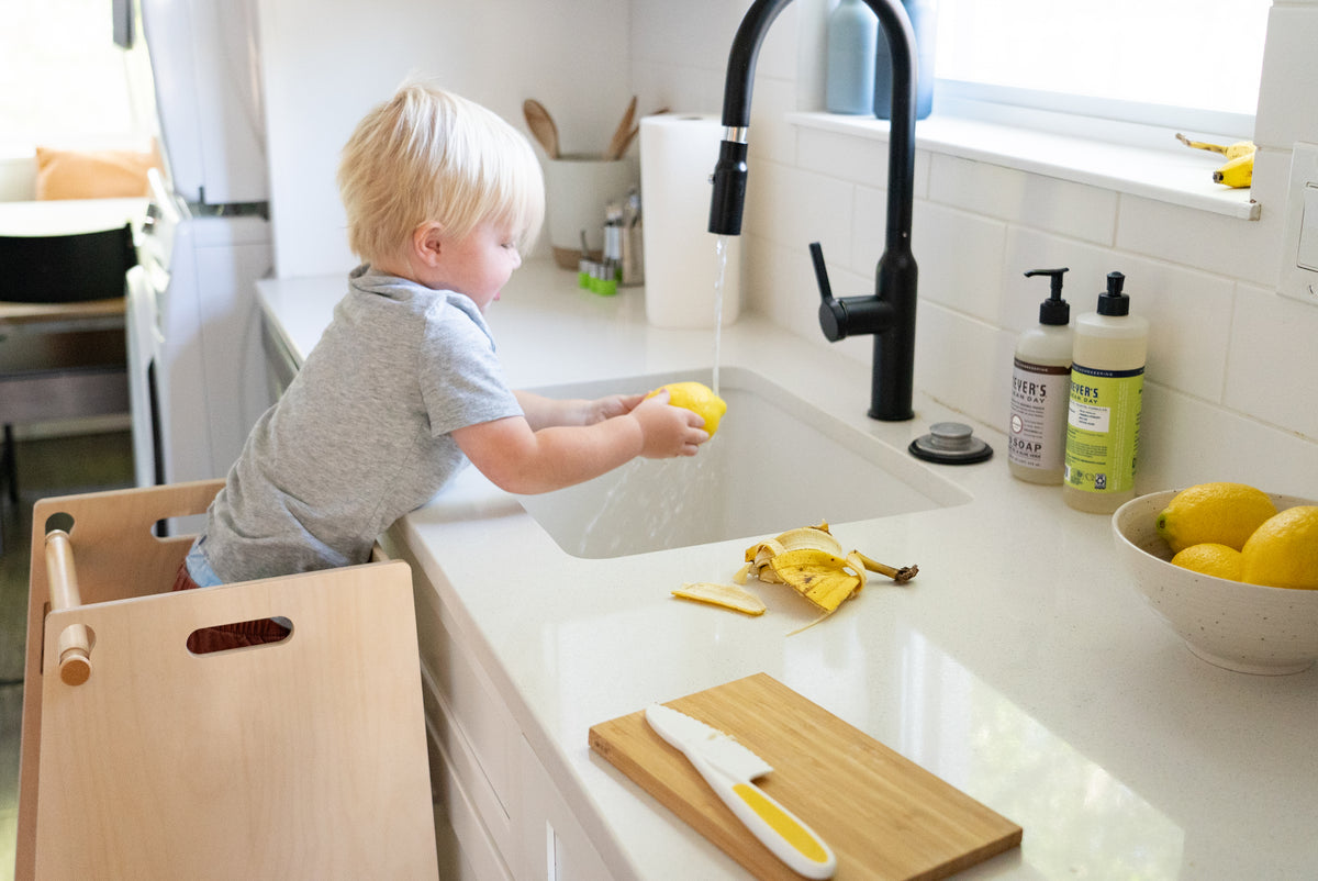young child helping wash fruit at kitchen sink