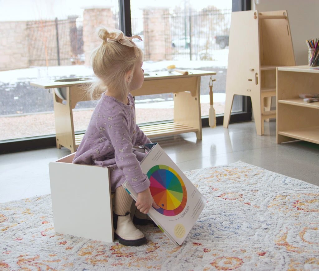 child in a Montessori classroom sitting in a flip chair with a book