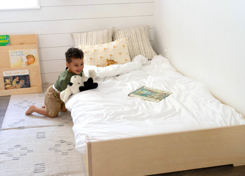 a toddler leaning on the edge of a twin floor bed 
