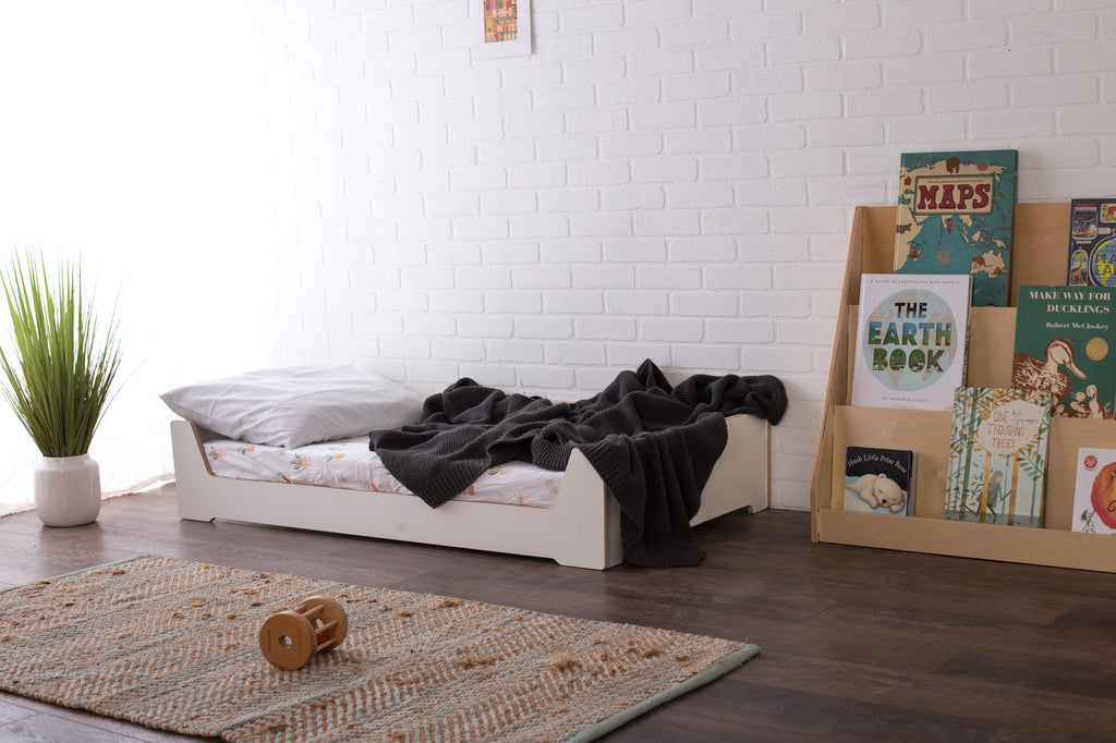 a white melamine crib size Montessori bed in a children's room