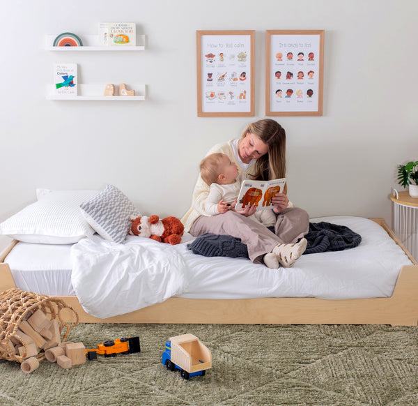 Woman reading a book to a child on a floorbed in a child's bedroom.