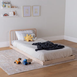 Children's bedroom with a wooden toddler floor bed, toys, and decorative elements.