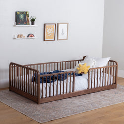 Wooden Floor Bed with High Rails with bedding and toys in a room with a rug and wall decorations.