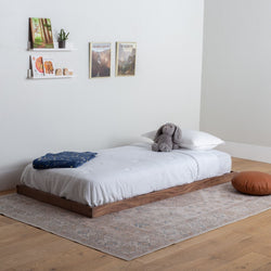 Wooden platform bed with white bedding and a small plush toy in a minimalistic bedroom.