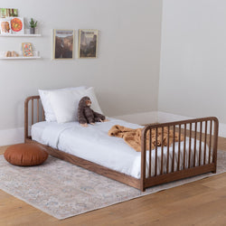 Children's wood bed frame, white mattress, and blanket in a room setting.