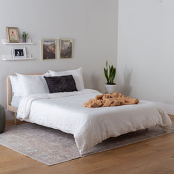 solid wood bed with white bedding and a brown throw blanket in a bedroom setting.