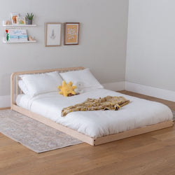 Wooden low kids bed with curved headboard, white bedding and stuffed plushes in a room with a shelf and framed pictures.