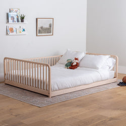 Big kid bed with white bedding and stuffed animals in a room with wooden flooring and a shelf.