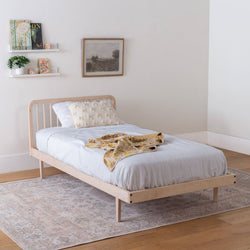 Wooden kids' bed with white bedding and a yellow blanket in a room with a rug and wall decor.