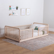 Wooden montessori bed with white bedding in a room with a rug and wall decorations.