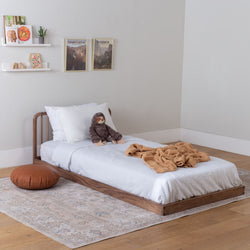 Walnut kids' bed with white bedding in a bedroom setting. 