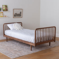solid wood kids' bed with white bedding with a footboard in a bedroom setting. 