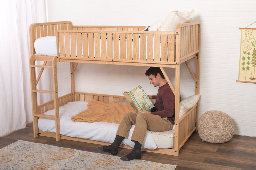 a dad sits on the bottom bunk of the low bunk bed and reads to his child
