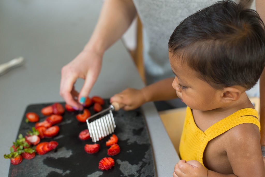 toddler standing at counter using crinkle cutter to cut strawberries