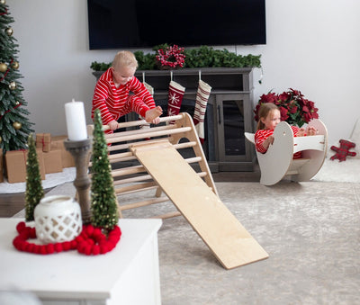 Children playing with a wooden climbing toy in a living room decorated for Christmas.