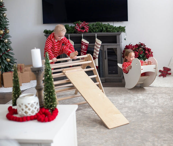 Children playing with a wooden climbing toy in a living room decorated for Christmas.