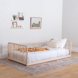 Wooden floor bed with high rails, white bedding, and a blanket in a room with a rug and wall decor.