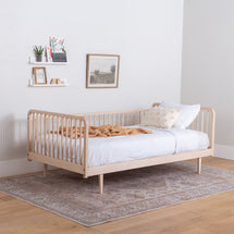 Wooden daybed with white bedding in a room with a rug and wall decorations.