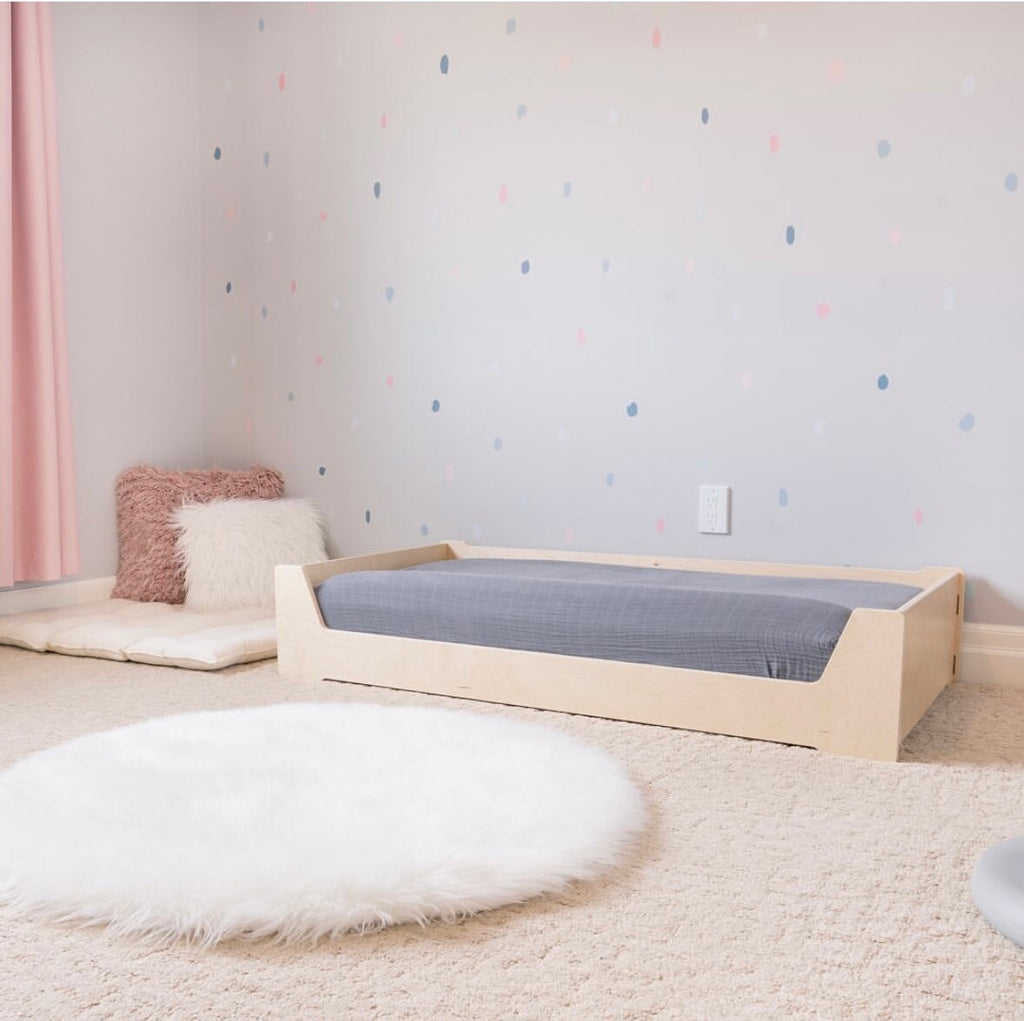 Children's room with a wooden floor bed, pink curtain, and colorful polka dot wall.