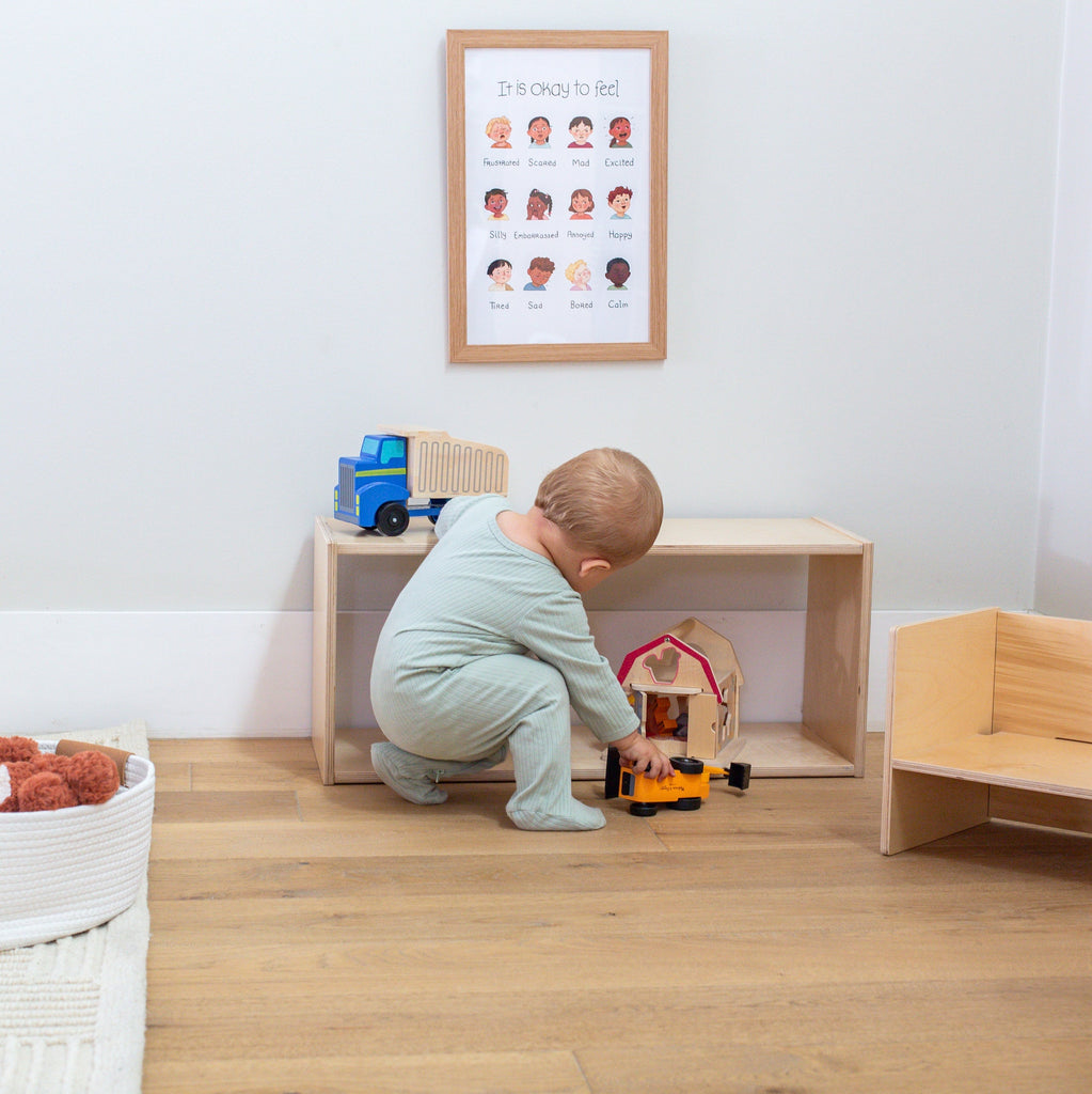 Baby playing with toys in a room with wooden furniture and a framed poster on the wall.