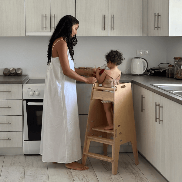 A woman and child using a toddler tower in the kitchen.