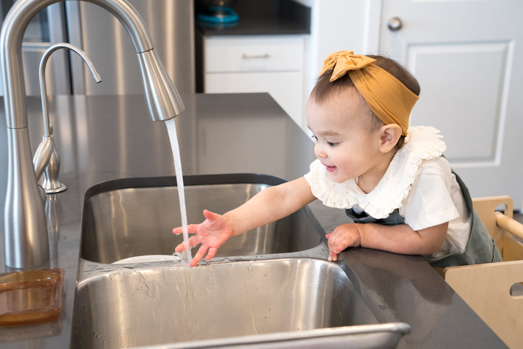 toddler using a learning tower to wash hands at sink