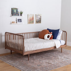 Wooden walnut daybed with rails white bedding and colorful pillows in a room with a rug and wall decor.