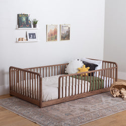 Wooden floor bed with rails with white bedding and pillows in a room with framed pictures on the wall.