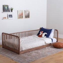montessori floor bed with rails in a low position, open from the side. The bed has pillows and a comforter. 
