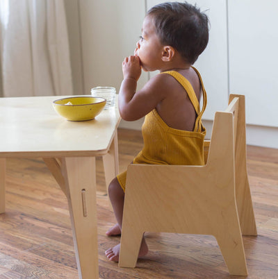 Child sitting at a wooden toddler table and chair set eating from a bowl. 