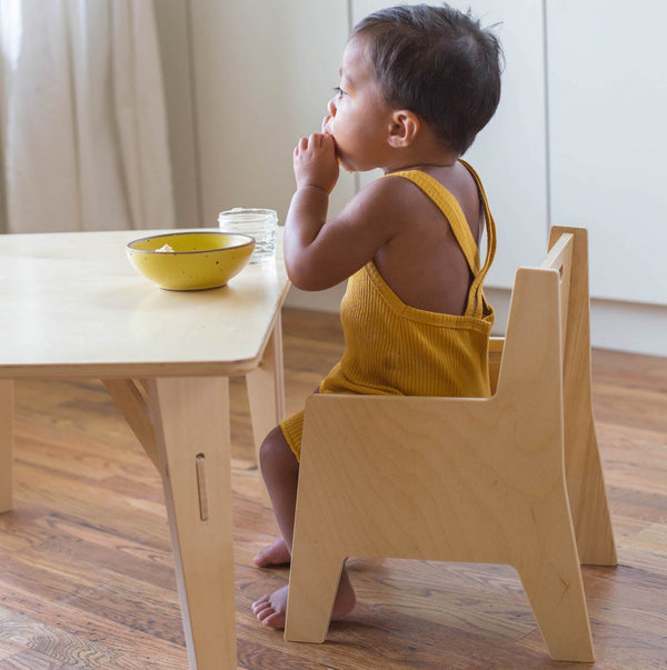 Child sitting at a low wooden table and chair eating. 