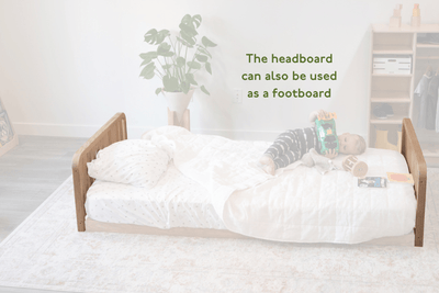 Child lying on a Toddler bed with a headboard, surrounded by white bedding and a plant in the background.