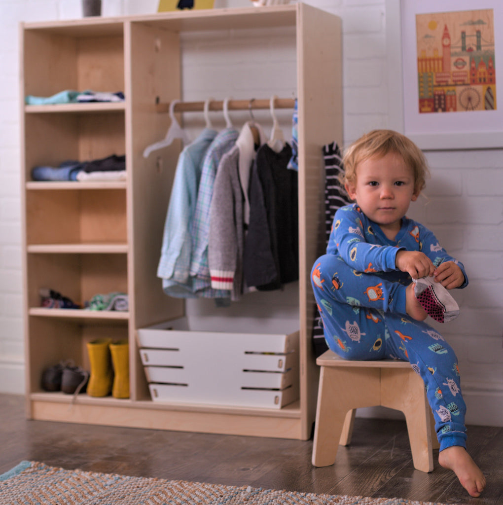 kids wardrobe filled with children's clothes and child putting on socks seated on a Stubby Stool.