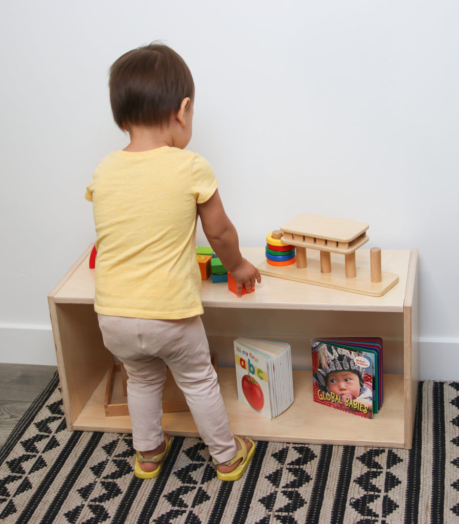 A little girl plays with wooden toys on a short infant shelf