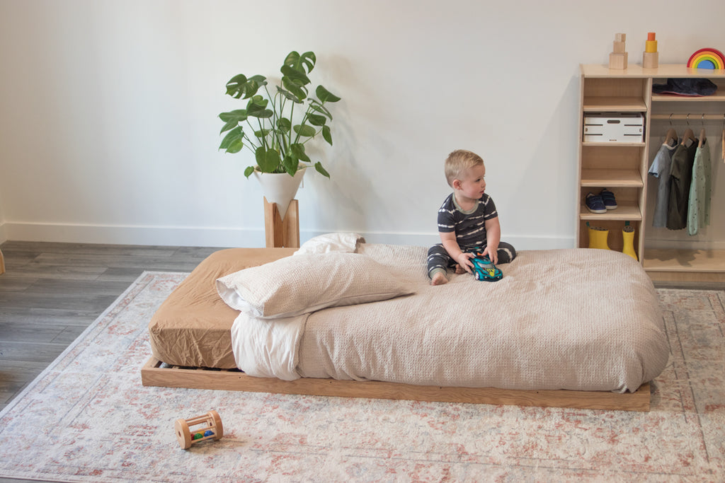 A little boy sits on the twin floor bed without rails